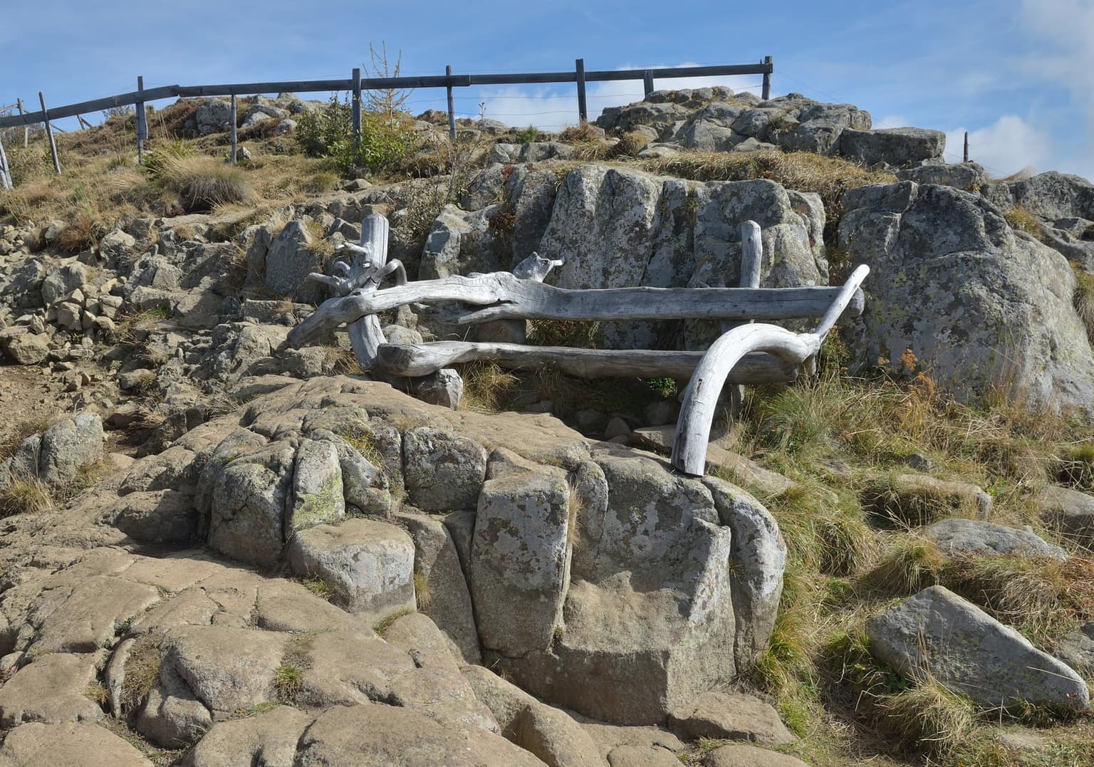 The Witches' Benches on Mount Bullaccia, paired weathered stone armrests and backrests forming a natural double seat on a rocky ridge, with a wooden trail fence and open sky behind