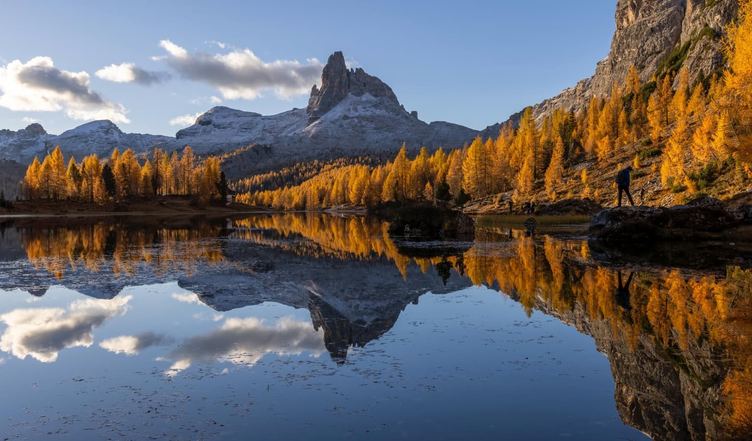 Autumn at Lago Federa, orange larches and the snow-dusted spire of Becco di Mezzodì mirrored in the still lake, a gray cliff wall rising on the right