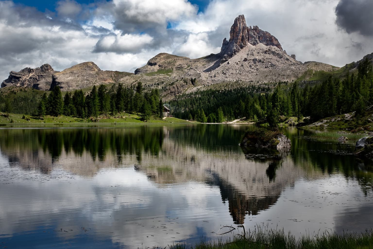 Conifers ringing a still alpine lake with a rocky pinnacle peak reflected in the water on the Croda da Lago circuit.