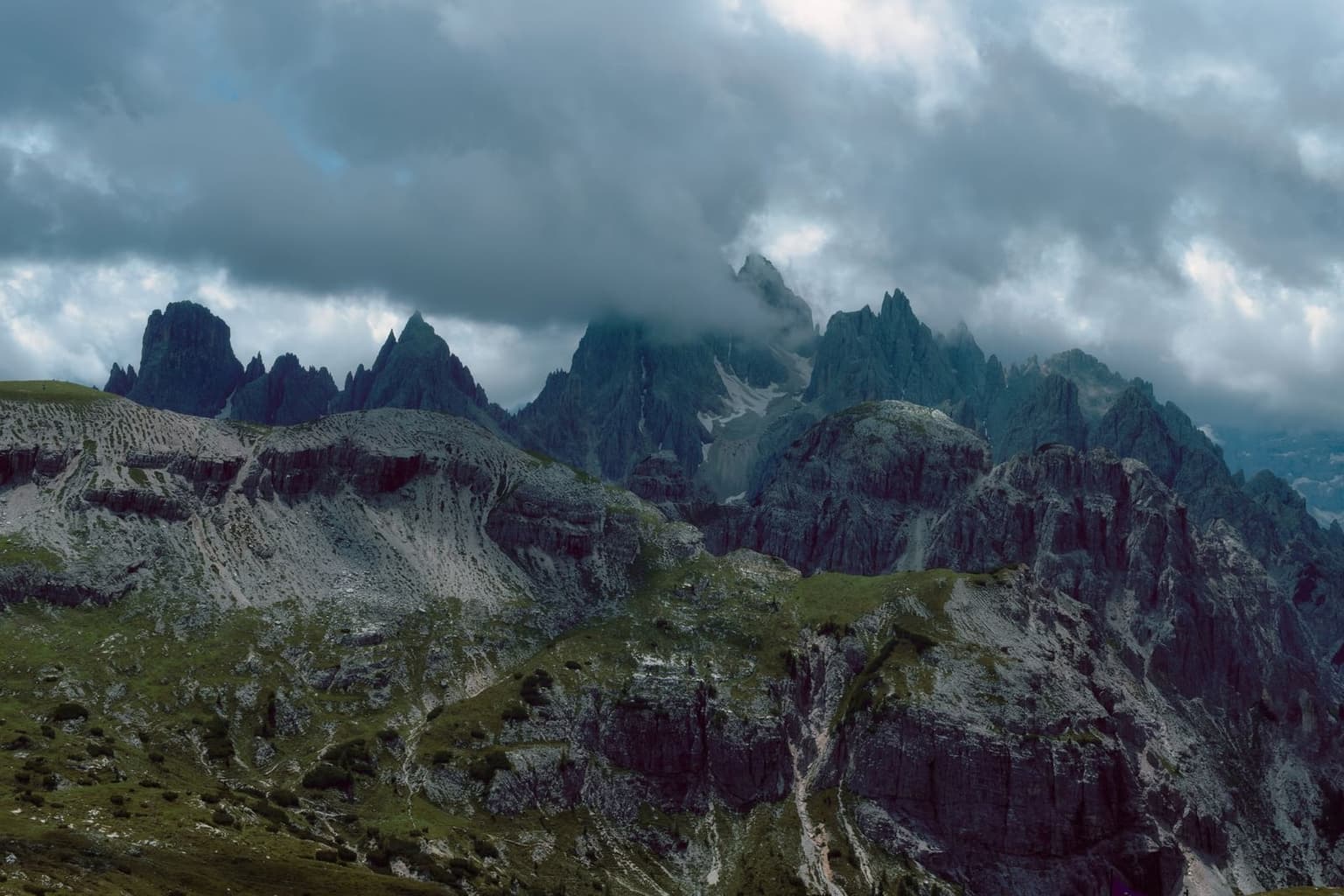 Dark thunderstorm clouds building over jagged, snow-free Dolomite peaks, seen from a high trail.