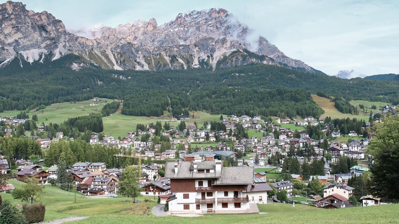 The town of Cortina d'Ampezzo spread across the green Ampezzo basin, with pale Dolomite peaks rising directly behind it in summer.
