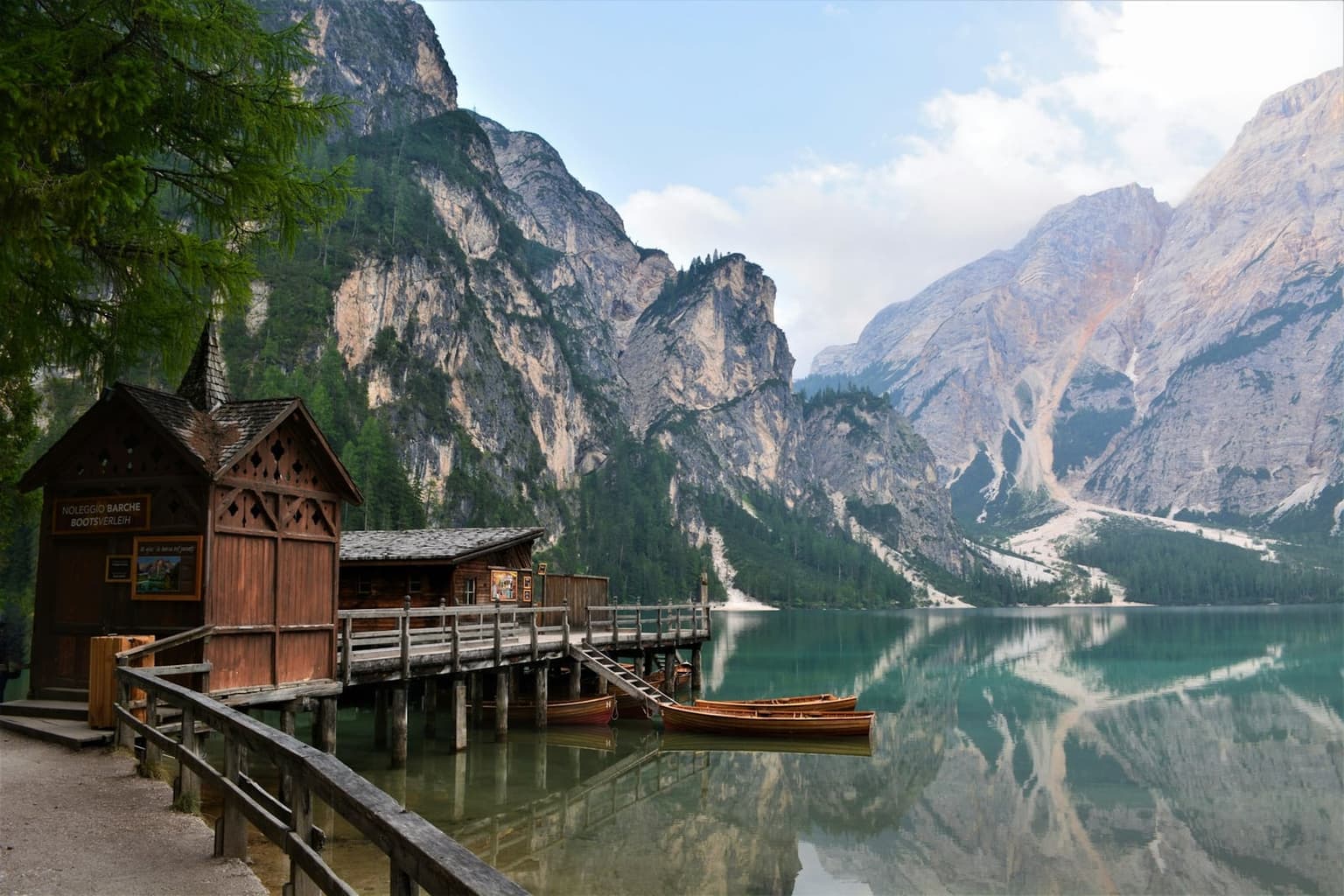 The wooden boat-rental hut at Lago di Braies, signed "Noleggio Barche / Bootsverleih," with rowboats moored below and the Dolomite peaks mirrored in turquoise-green water