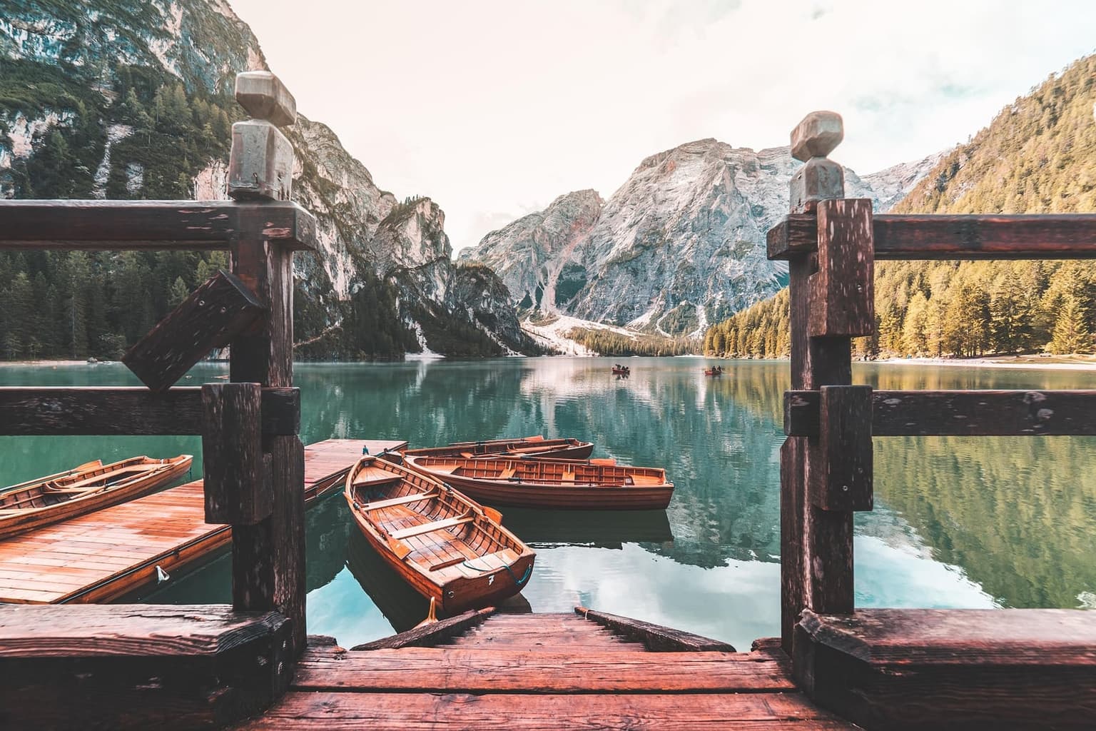 Traditional wooden rowboats moored at the boathouse dock on Lago di Braies, turquoise water reflecting the jagged gray wall of the Croda del Becco behind