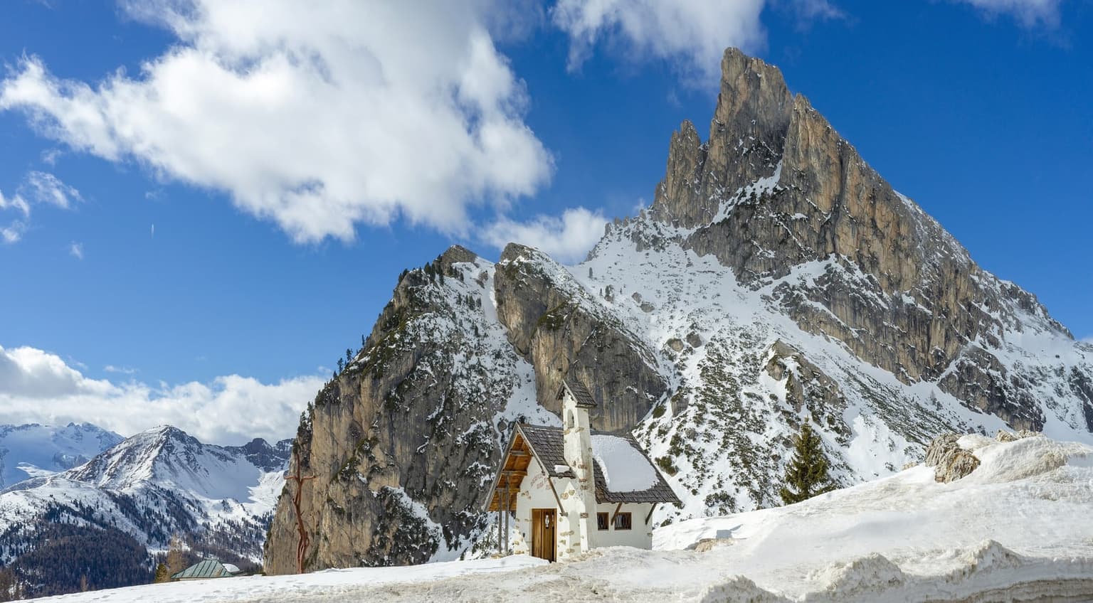 The small white chapel at Passo Falzarego in snow, under the rock face of Sass de Stria