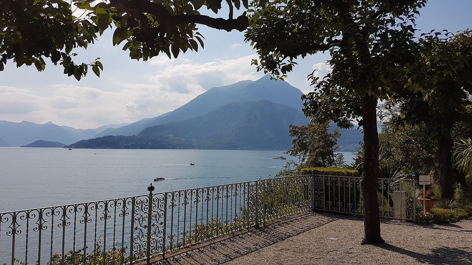 A wrought-iron balustrade on the lakeside terrace of Villa Cipressi in Varenna, looking out over Lake Como to the mountains