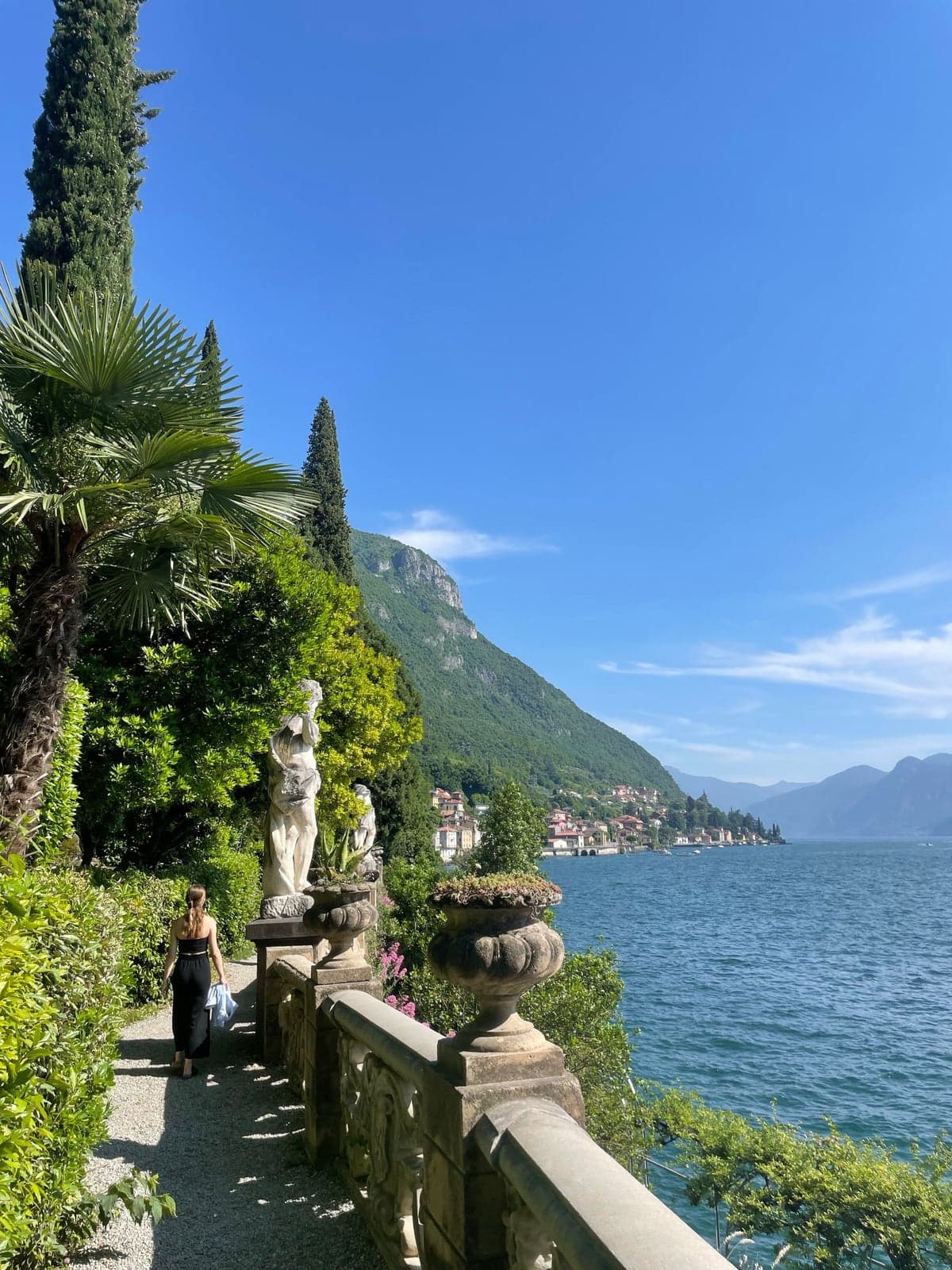 The lakefront botanical garden path at Villa Monastero in Varenna, statues and stone urns along a balustrade above the water