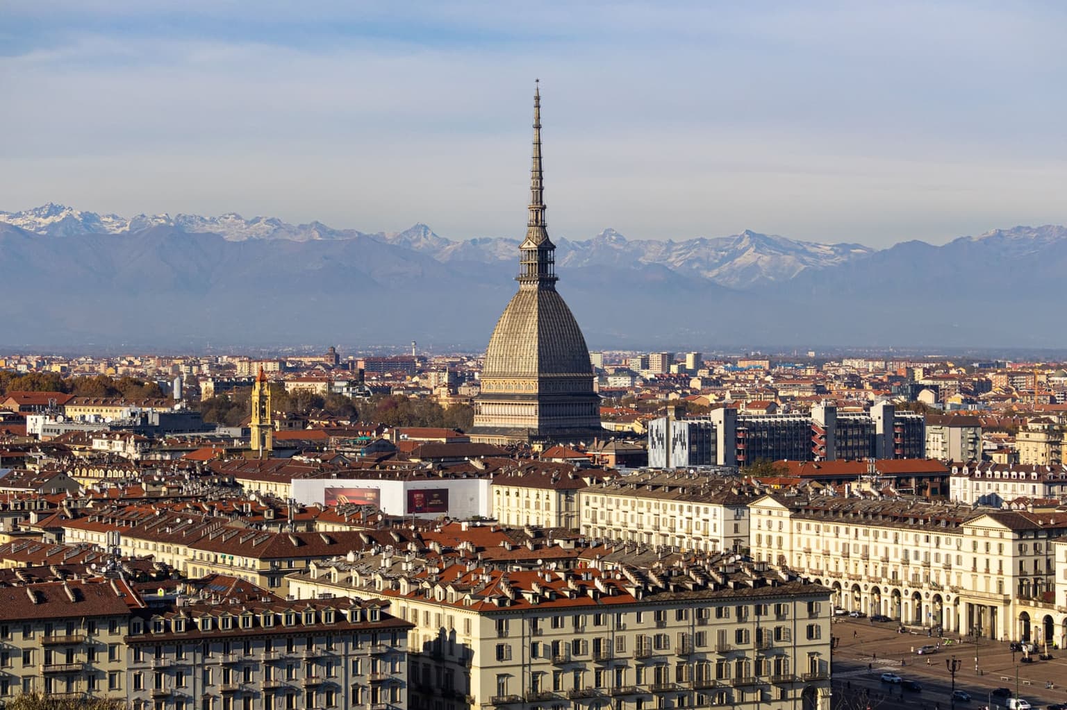 The Mole Antonelliana's tall spire over Turin's rooftops, with a long range of snow-capped Alps behind the city
