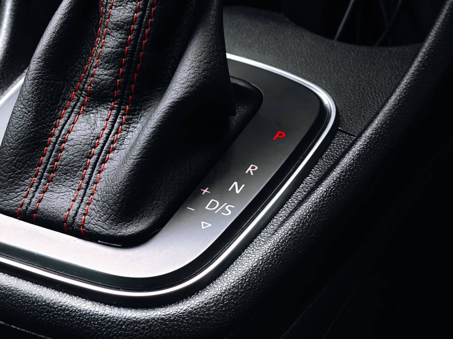 Close-up of an automatic gear selector in a small car, with P, R, N and D lit on the console plate and a black leather boot with red stitching.