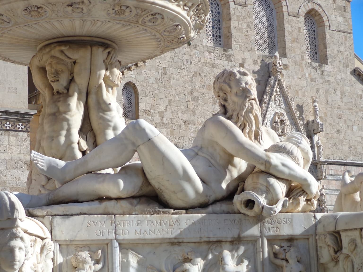 A reclining river-god figure on the Fontana di Orione, Messina's Renaissance fountain, with the Duomo's façade rising behind it