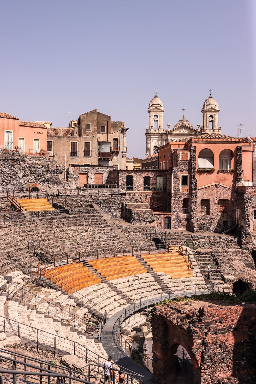 Catania's Roman Theatre seen from above, with apartment balconies rising directly behind the cavea