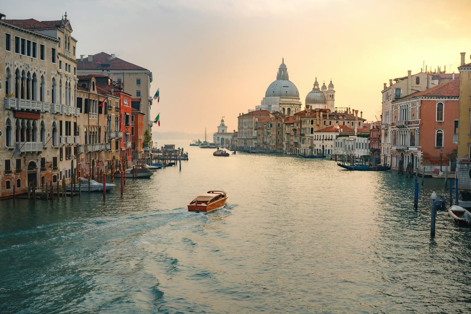 The Grand Canal in soft golden light, nearly empty except for one wooden motorboat, lined with old palazzos and leading to the domes of Santa Maria della Salute in the distance